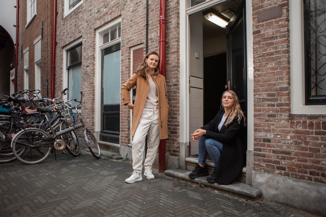 Twee meiden staan en zitten bij een deuropening.