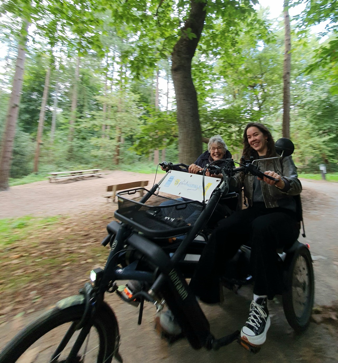 Nienke van Pel zit samen met een van de bewoners van een zorgcentrum op een duofiets voor een rit door de bossen.