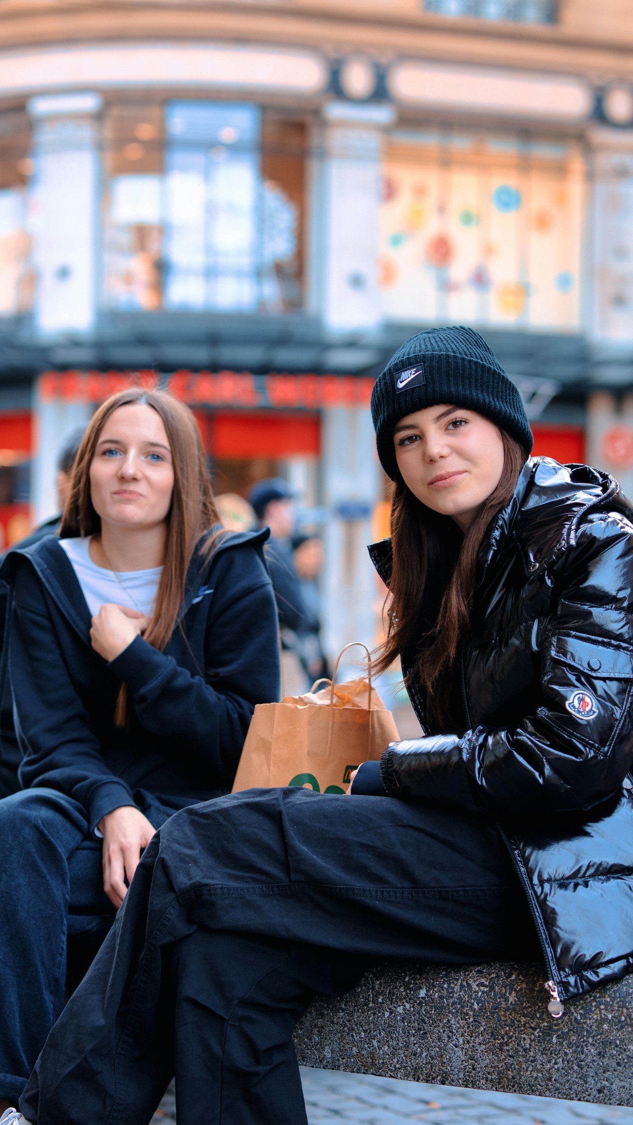 Twee jongeren zitten bij elkaar op een bankje voor een winkel